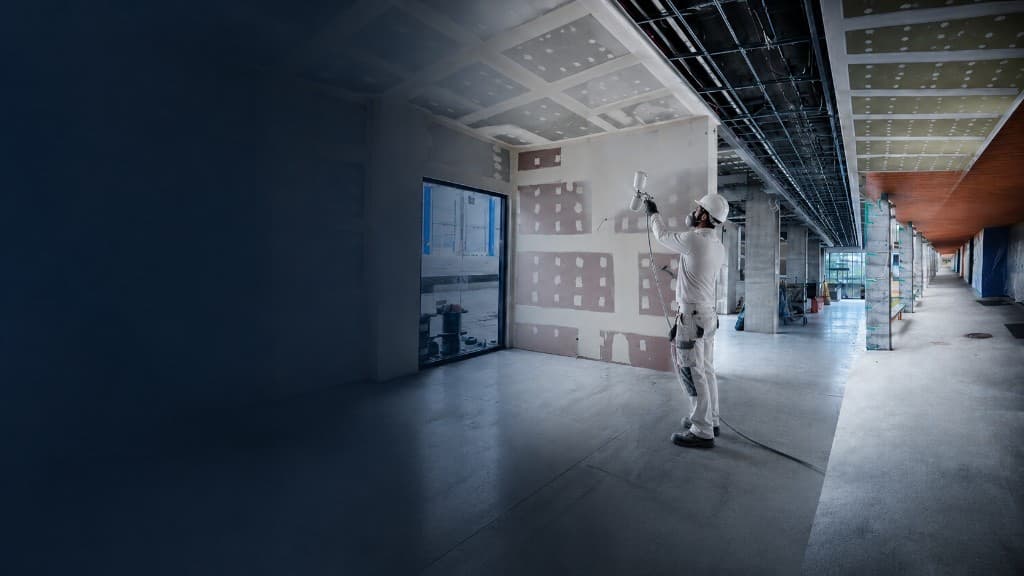 Commercial painter in protective gear spray-finishing a large interior site
